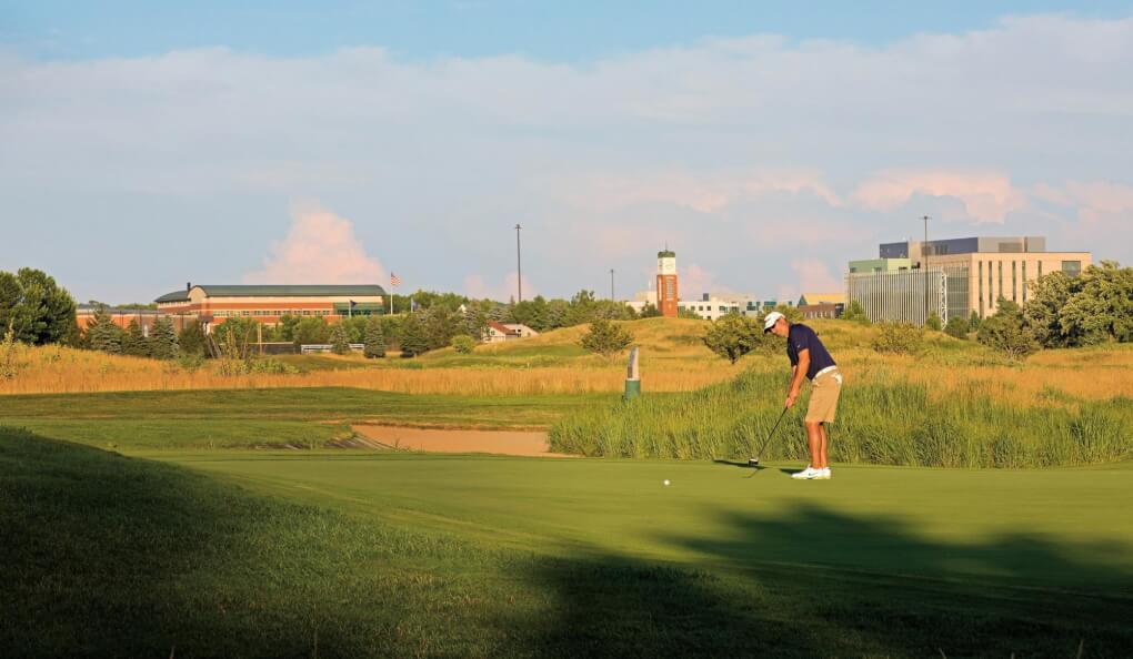 A golfer putts with a view of campus from the Meadows behind him.